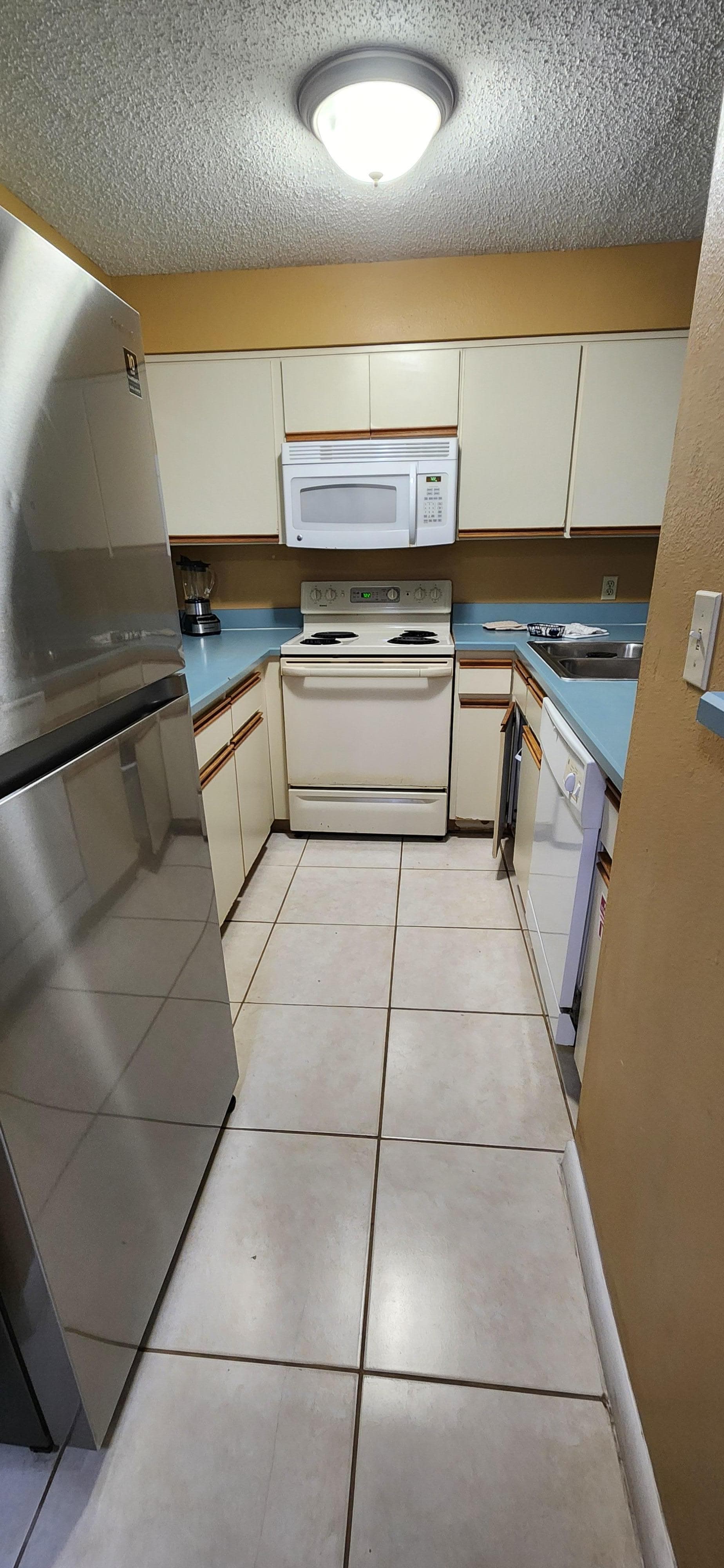 Kitchen with dented fridge, countertop and cupboard pieces missing. 