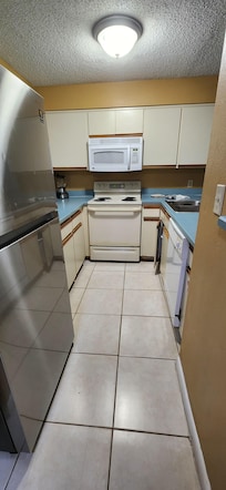 Kitchen with dented fridge, countertop and cupboard pieces missing.
