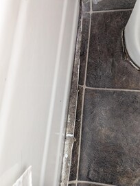 Peeling flooring next to bathtub.