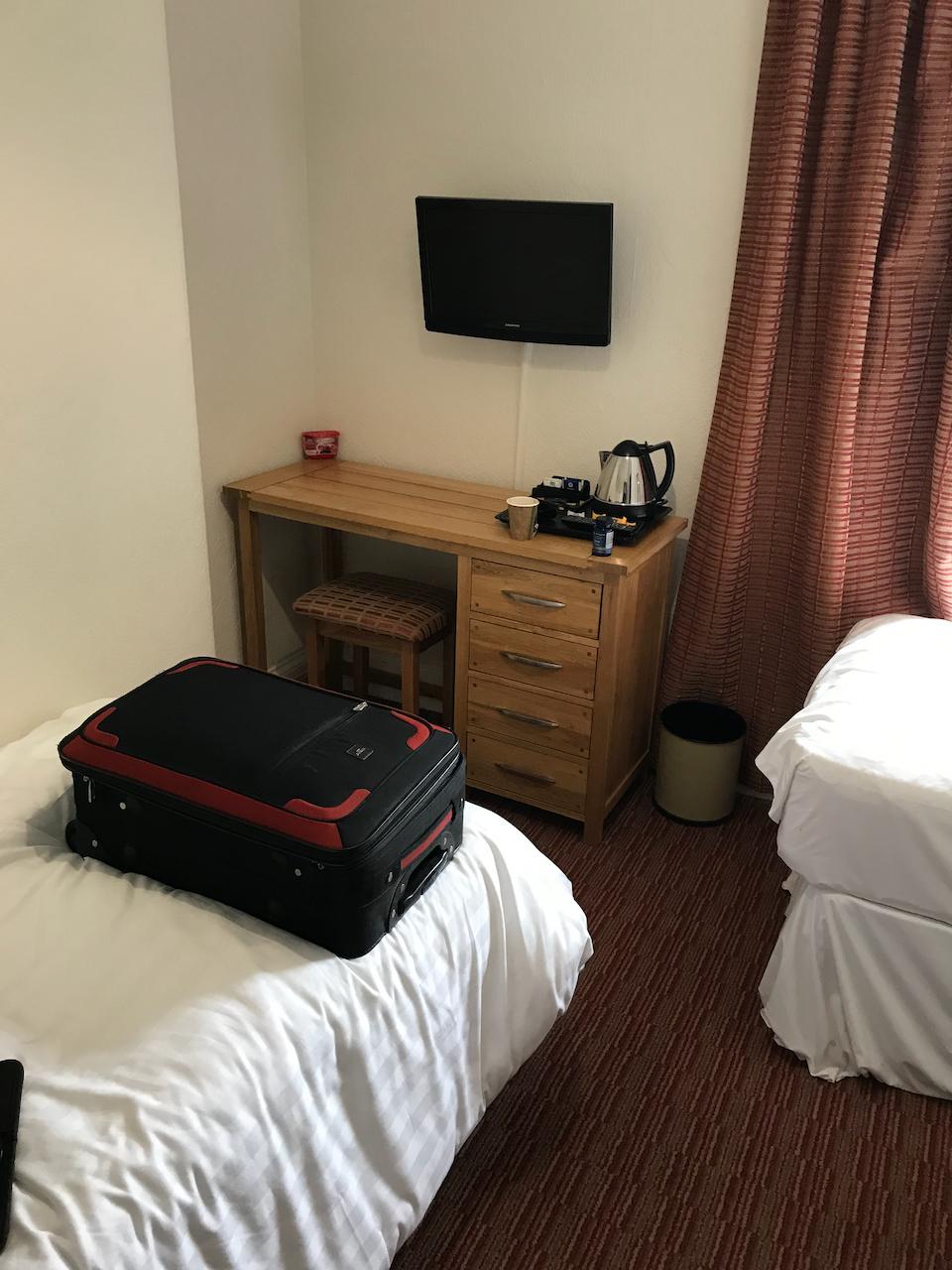 View of ends of both beds and refreshments + desk + TV.