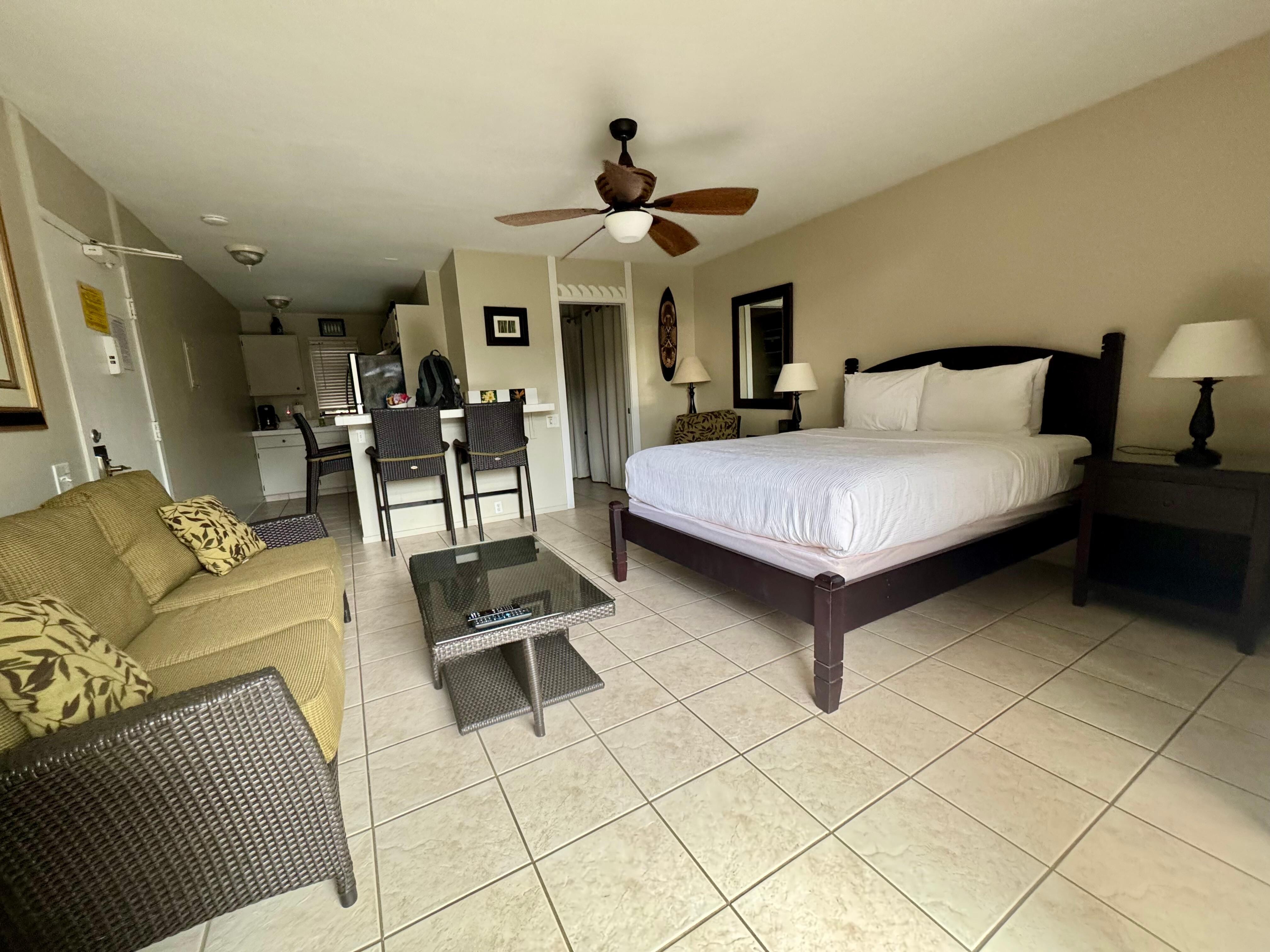 View of the studio condo queen size bed, bar, and full kitchen on the left side of the picture.