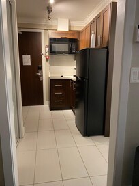 Looking from bedroom doorway to the kitchenette entrance area. Small hot plate style stovetop, full fridge, microwave, dishes, cutlery, pots, toaster and kettle provided.