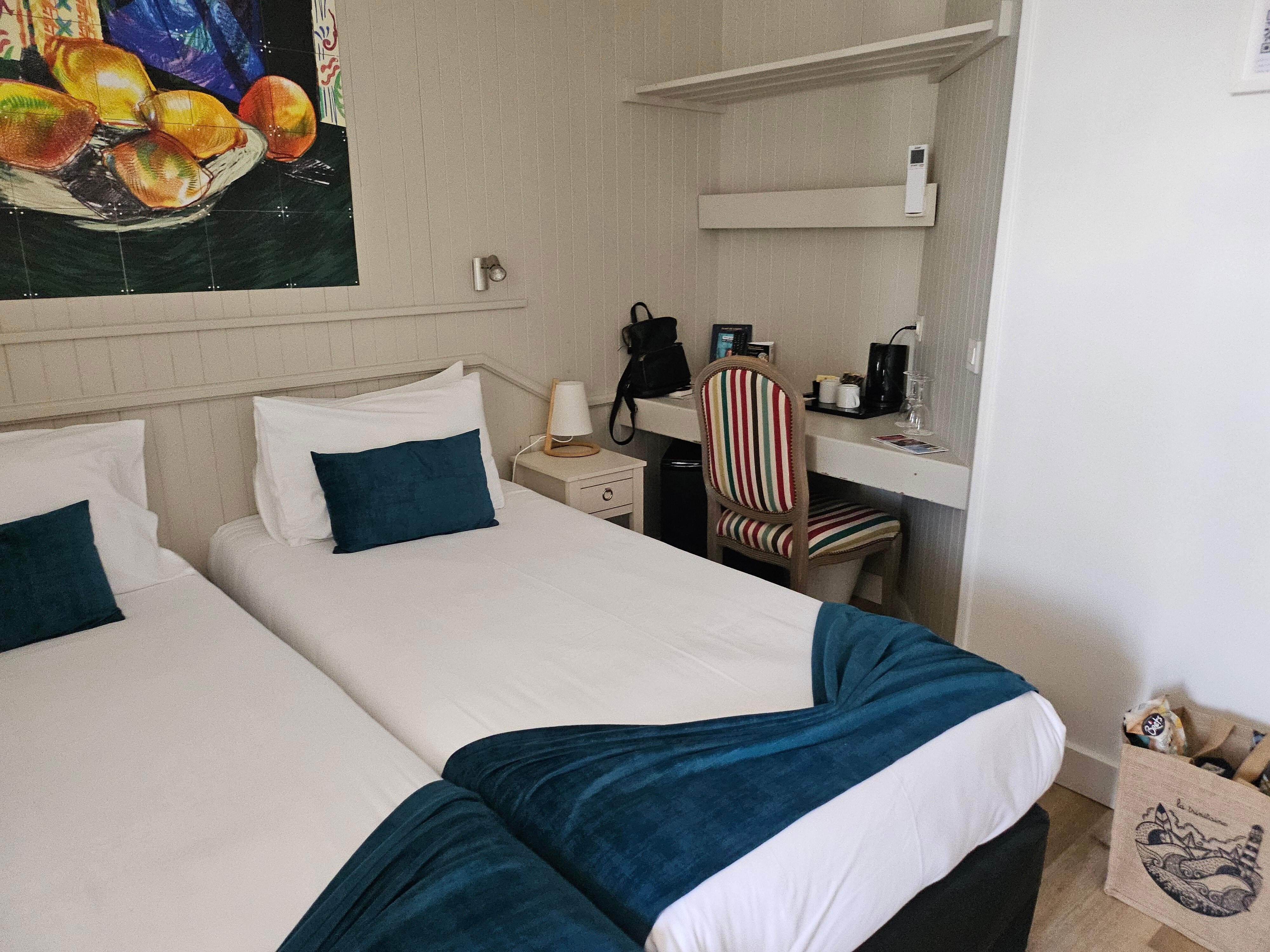 Comfy beds next to a desk, shelf, coffee maker, and minifridge.