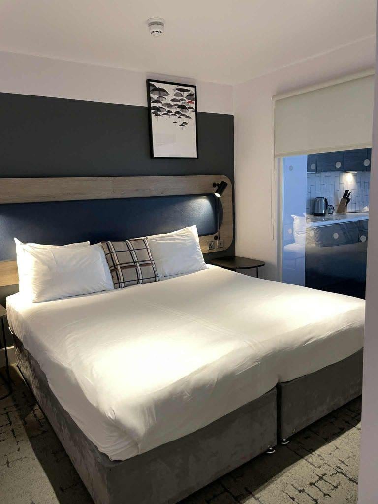 Dubbelsängen och man ser en del av vardagsrummet genom fönstret som skiljer rummen åt. 