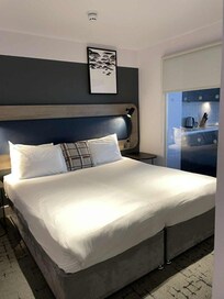 Dubbelsängen och man ser en del av vardagsrummet genom fönstret som skiljer rummen åt.