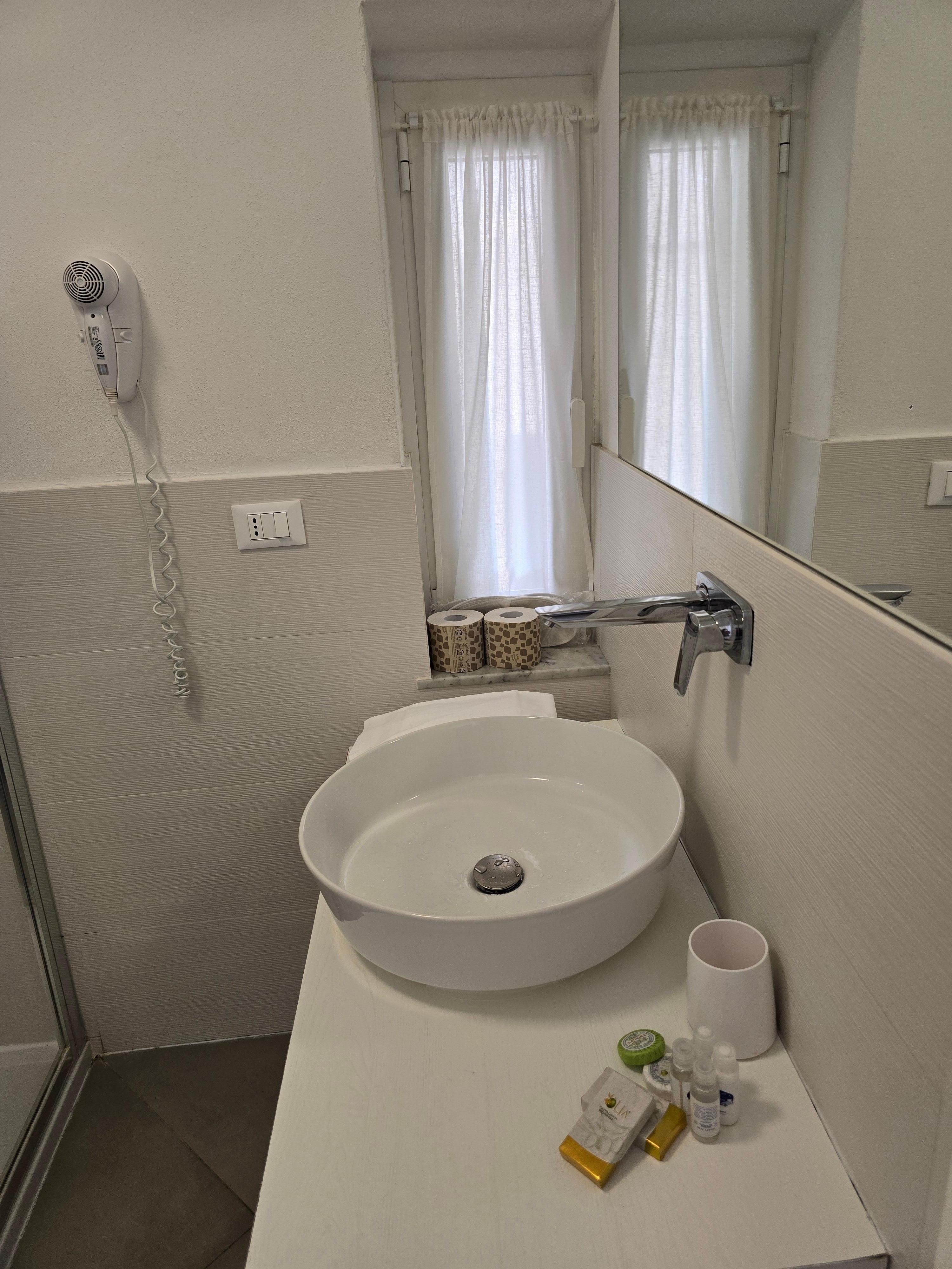 Romslig vask og vindu på badet, shampo og såpestykker og bodylotion, tøfler og dusjhette.