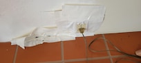Power plug held in the wall with athletic tape. More tape to the left covering hole in the drywall.