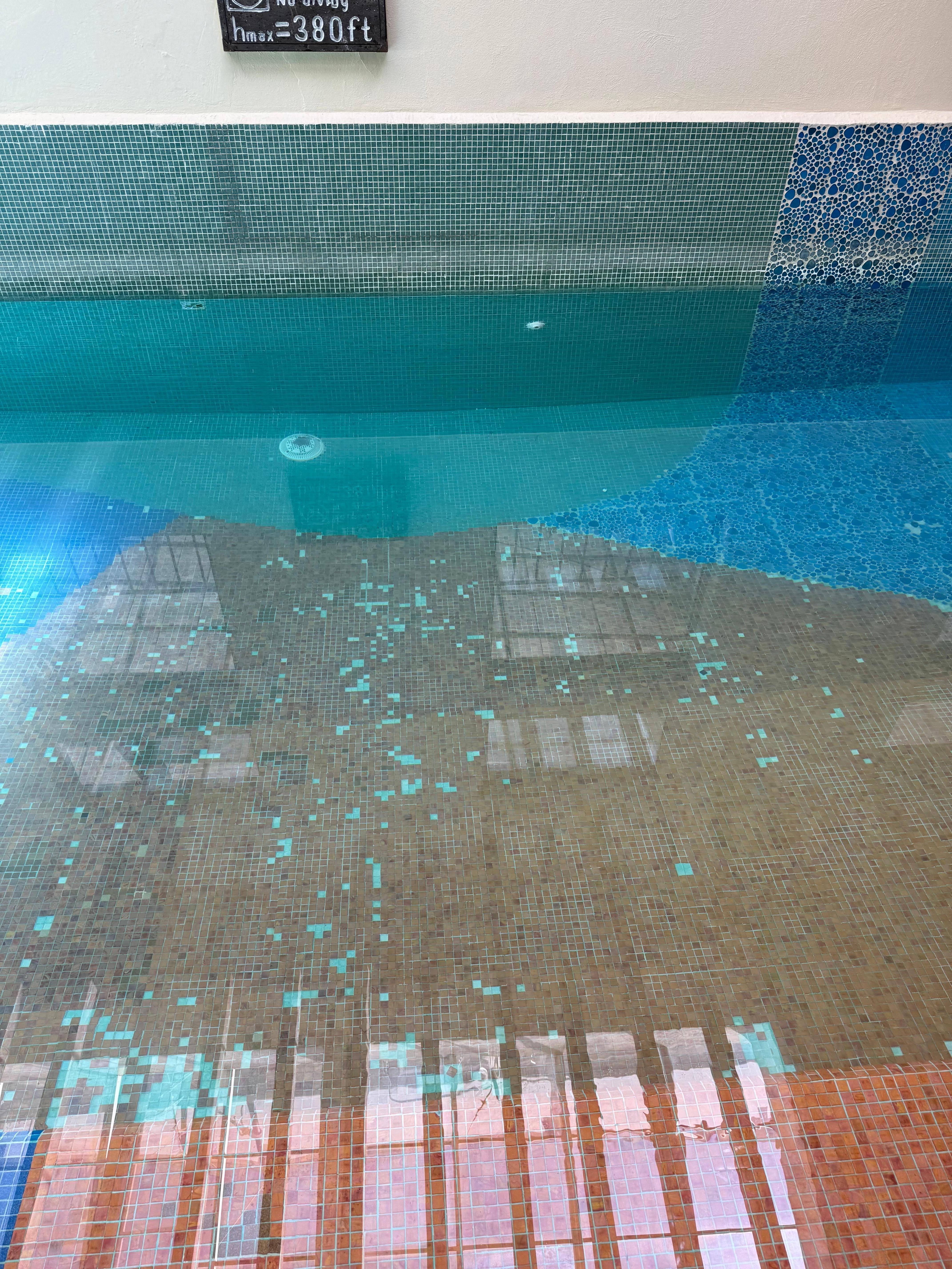 Alberca con mosaicos rotos y piedras en al fondo 