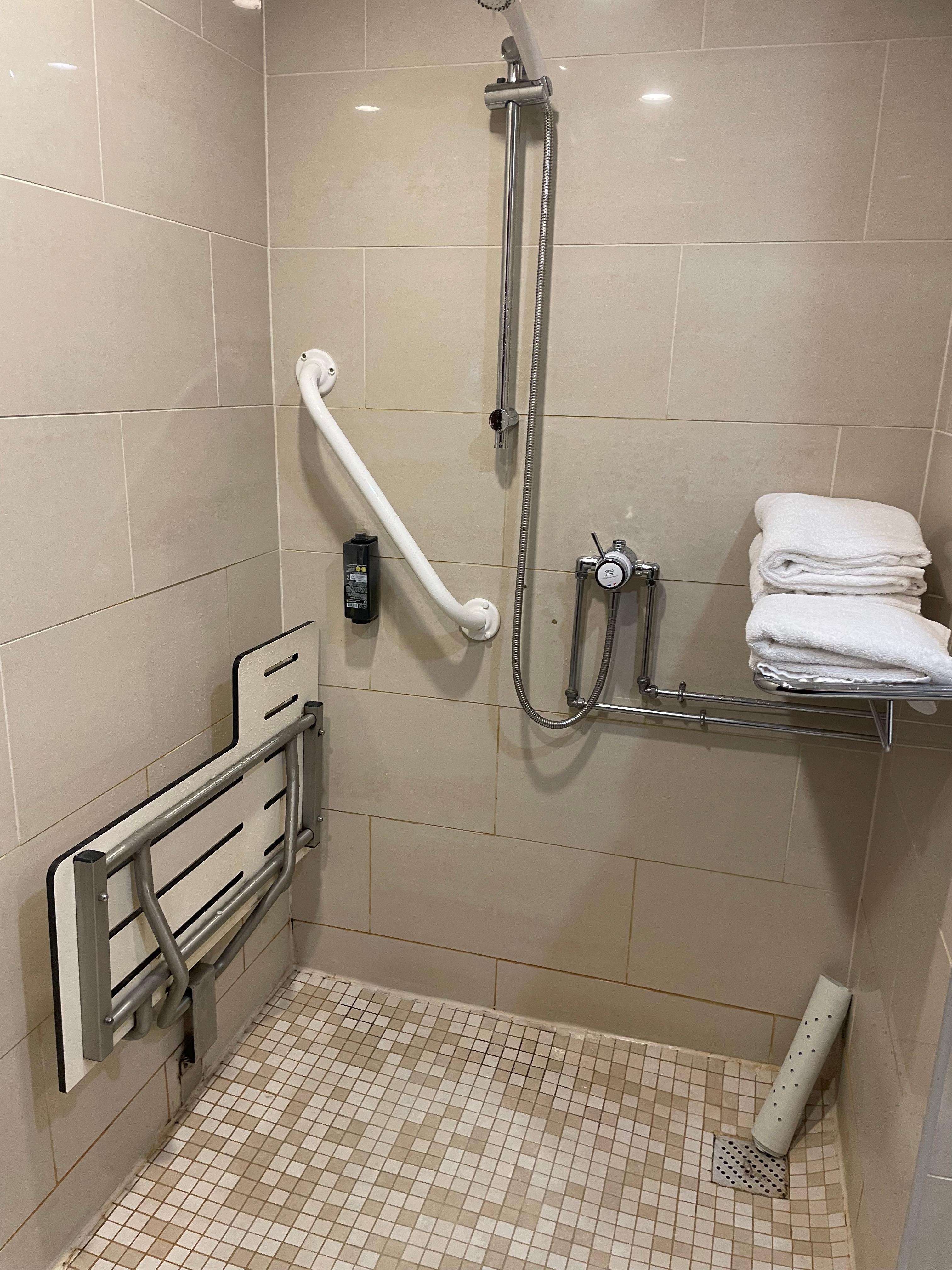 Outdated, stained shower in room 105 - accessible room. With towels in shower.