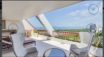 Online picture of balcony with nice plants and outdoor lounge chairs and table behind high back chairs.