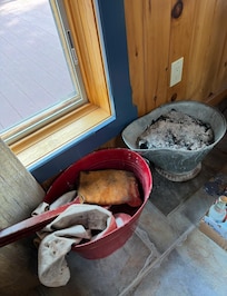 Open bucket of wood stove ashes and tools on the living room floor.