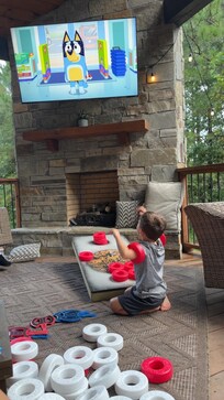 Our 4 yr old watching Bluey on the big screen outside while playing cornhole/connect 4