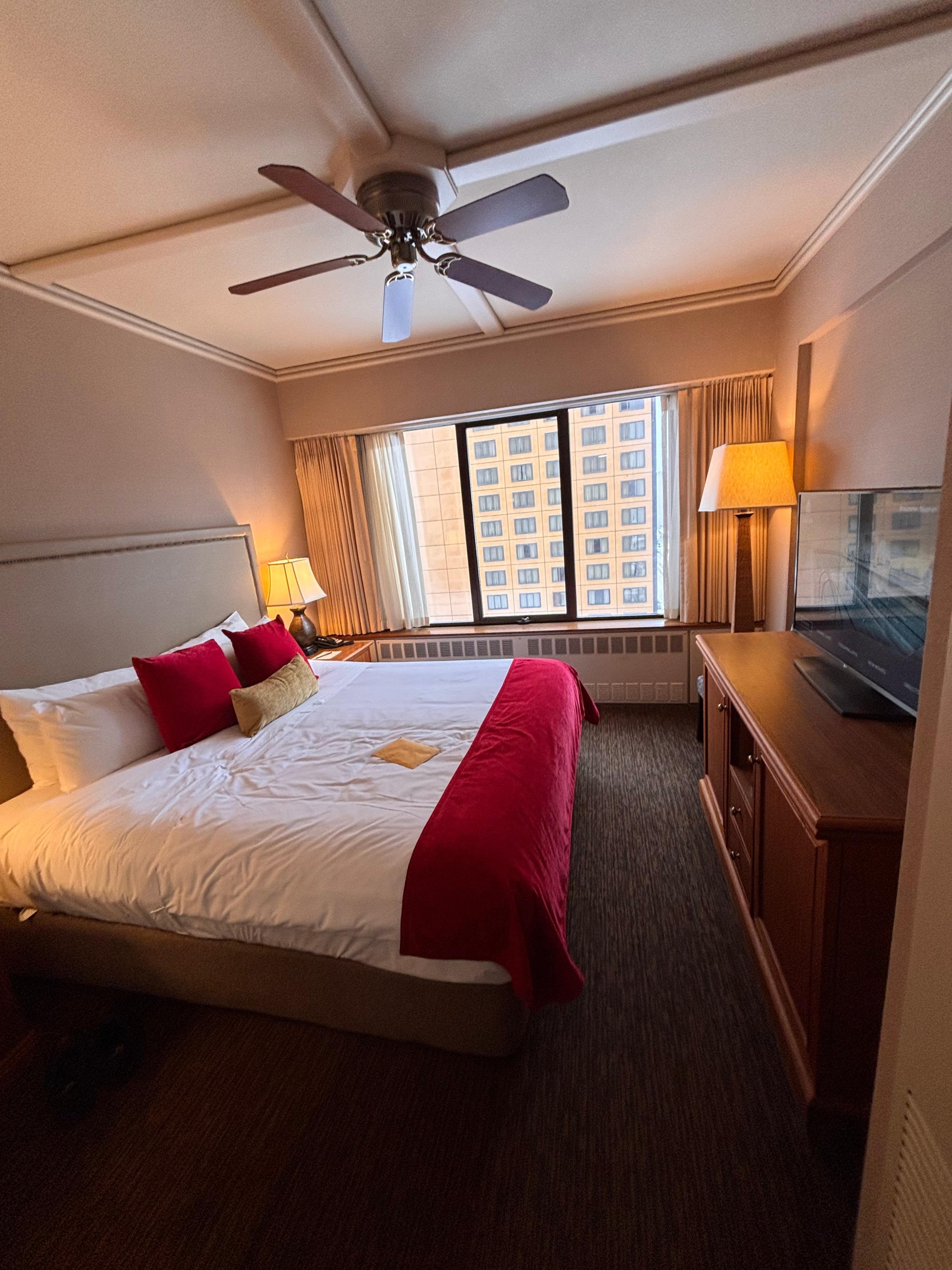 A comfortable bedroom includes a chest of drawers, small refrigerator  television and a enclosed closet. 