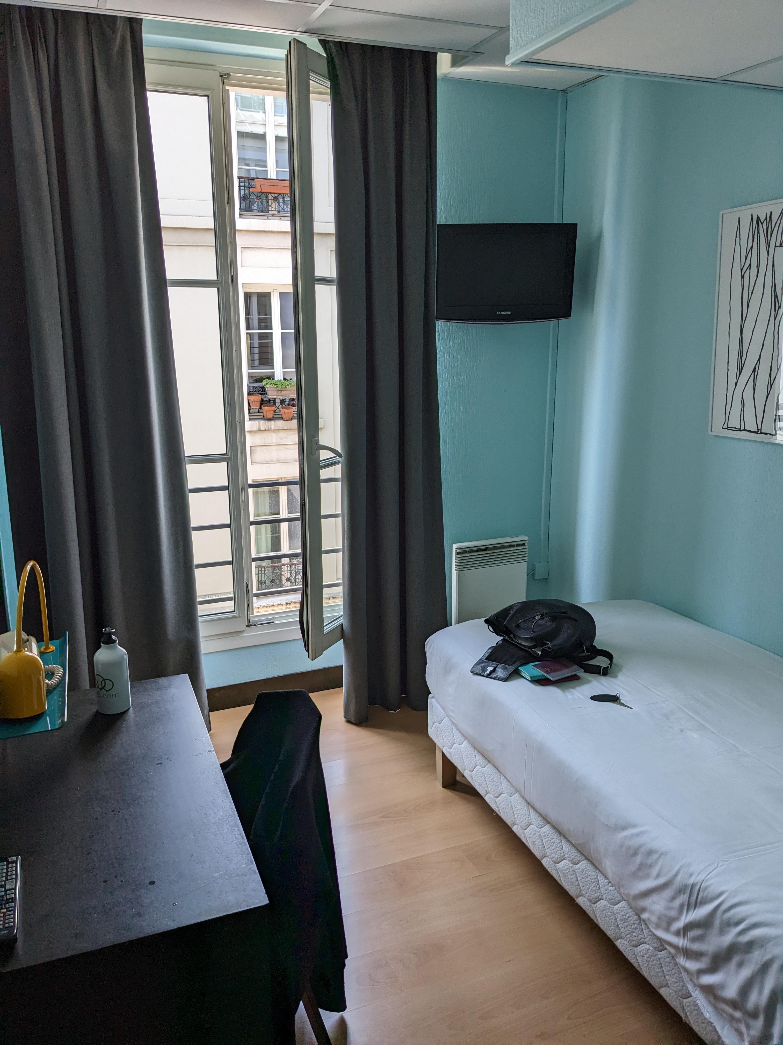 Single bed with desk and windows opening to the street. Space for a case and clothes hanging ( and a safe) beyond the desk. 