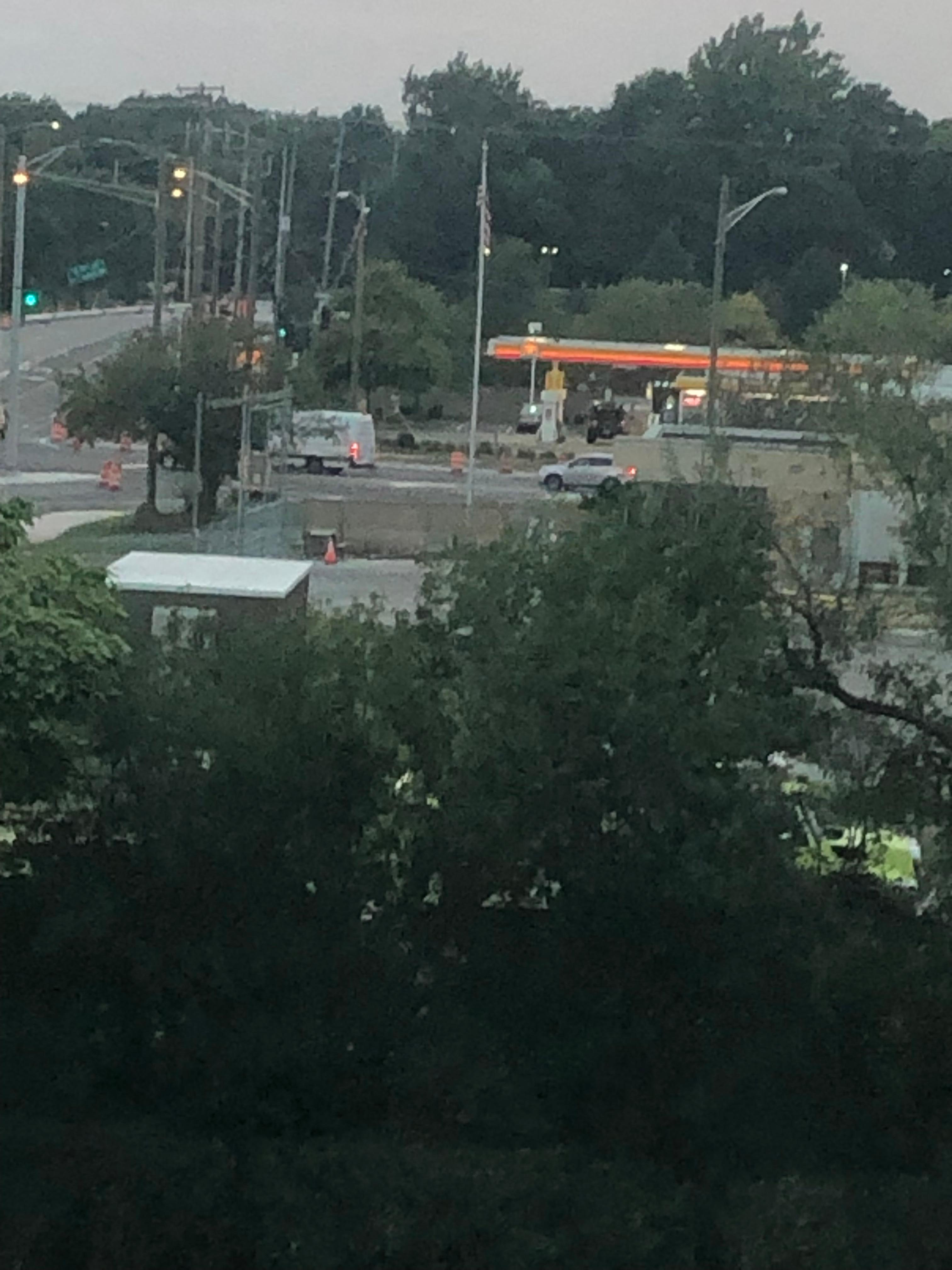 Une station-service Shell dans un lot de réverbères, entourées d'arbres verdoyants. 