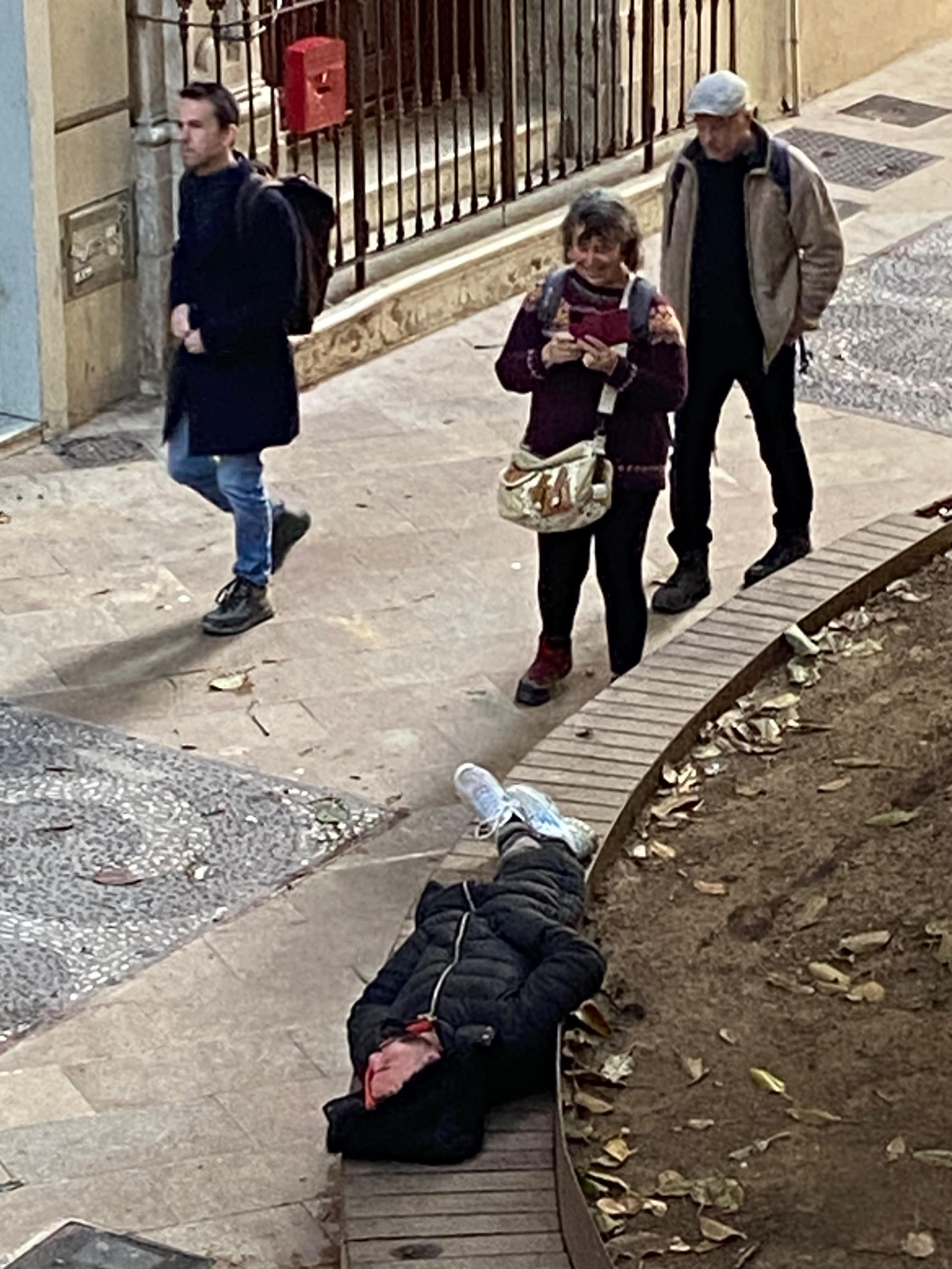 Locals walking by a sleeping homeless person sleeping in the plaza