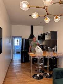 The kitchen, as seen from the living room and toward the bedroom at the back of the apartment, with oven, microwave, refrigerator, dishwasher, toaster, coffee maker. Four adjustable stools for use at the counter for eating.