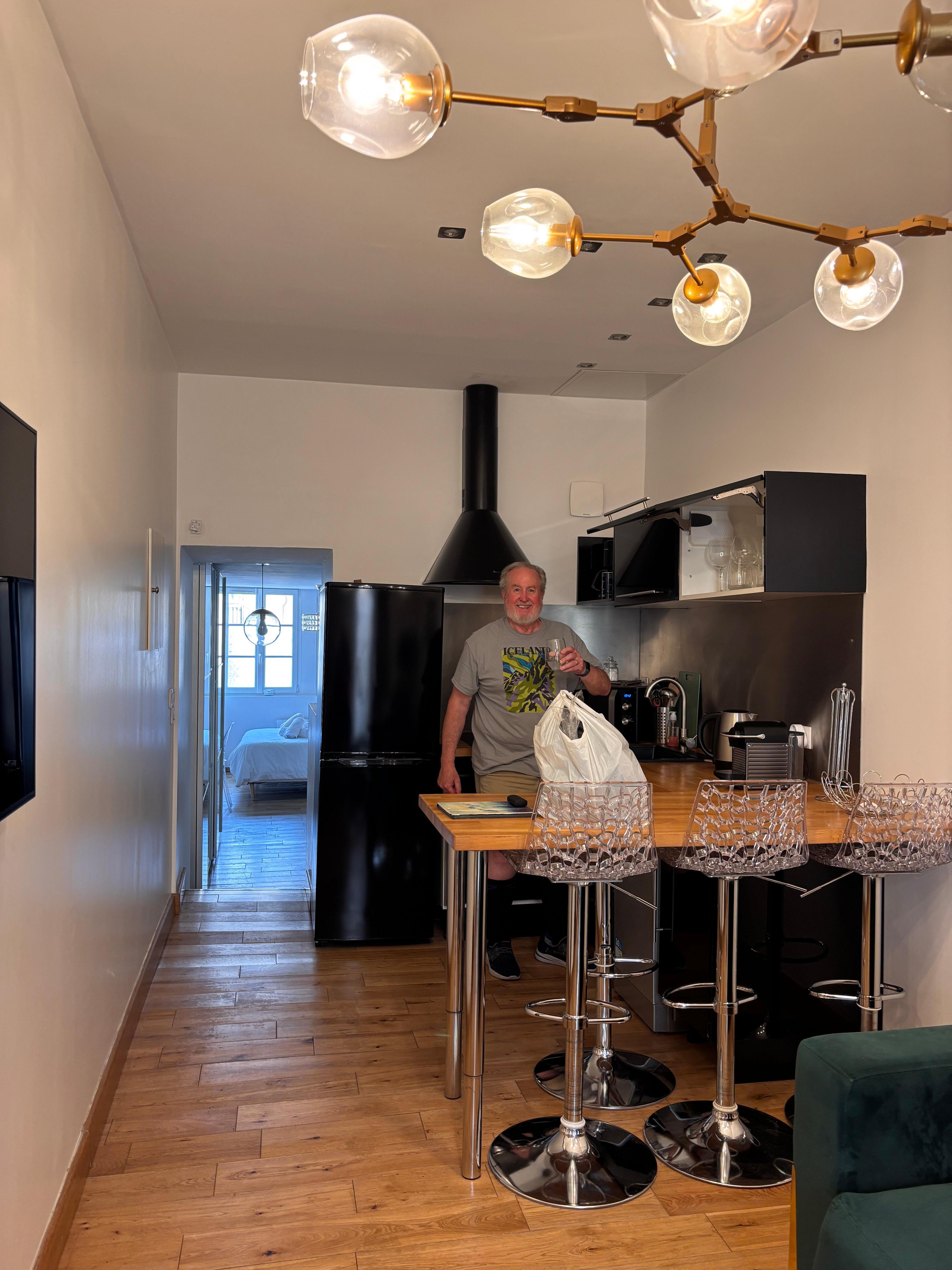 The kitchen, as seen from the living room and toward the bedroom at the back of the apartment, with oven, microwave, refrigerator, dishwasher, toaster, coffee maker. Four adjustable stools for use at the counter for eating.