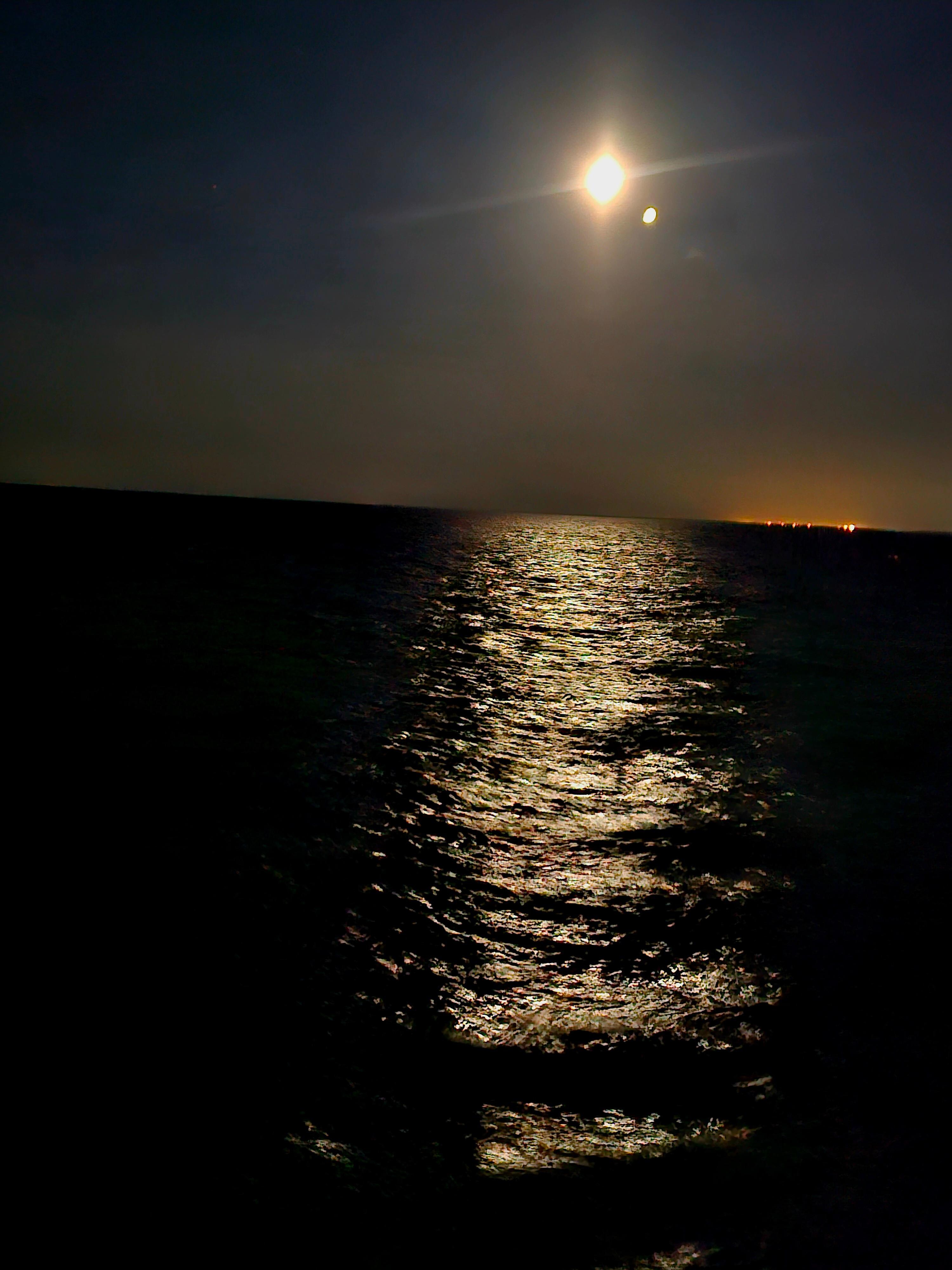 The luminous moon is positioned near the ocean.