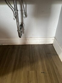 red substance ( possibly blood ) on baseboard under the sink