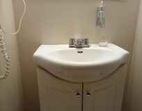 The sink is in a separate room from the toilet and shower. Wall hanging hair dryer is on the left. Soap dispenser is attached to the wall above the sink.