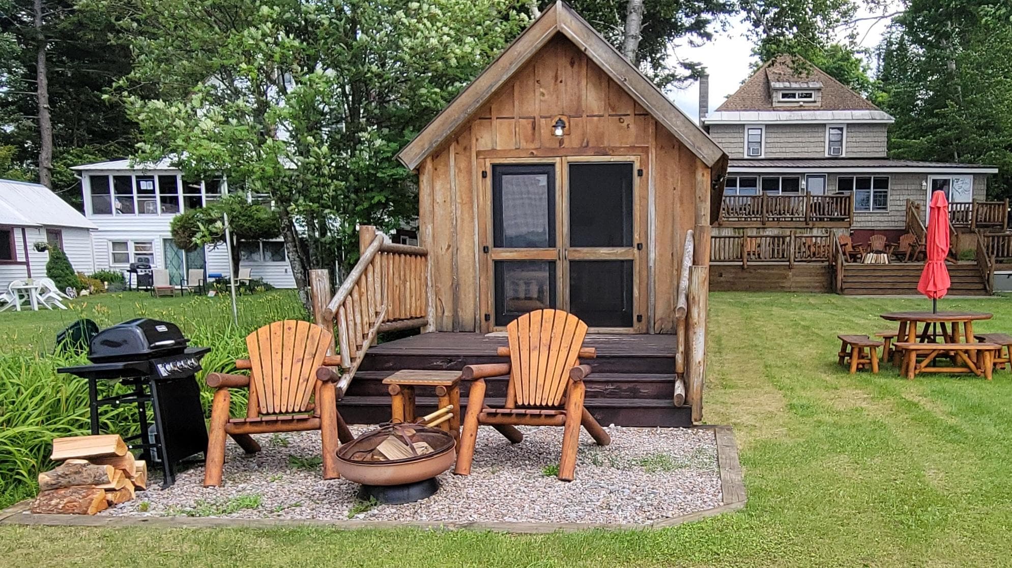 Front view of the cabin, equipped with a grill, fireplace, and wood.