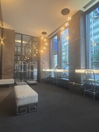 A lounge-style space with benches, high stools, and large windows letting in natural light. Hanging lights add a modern touch.