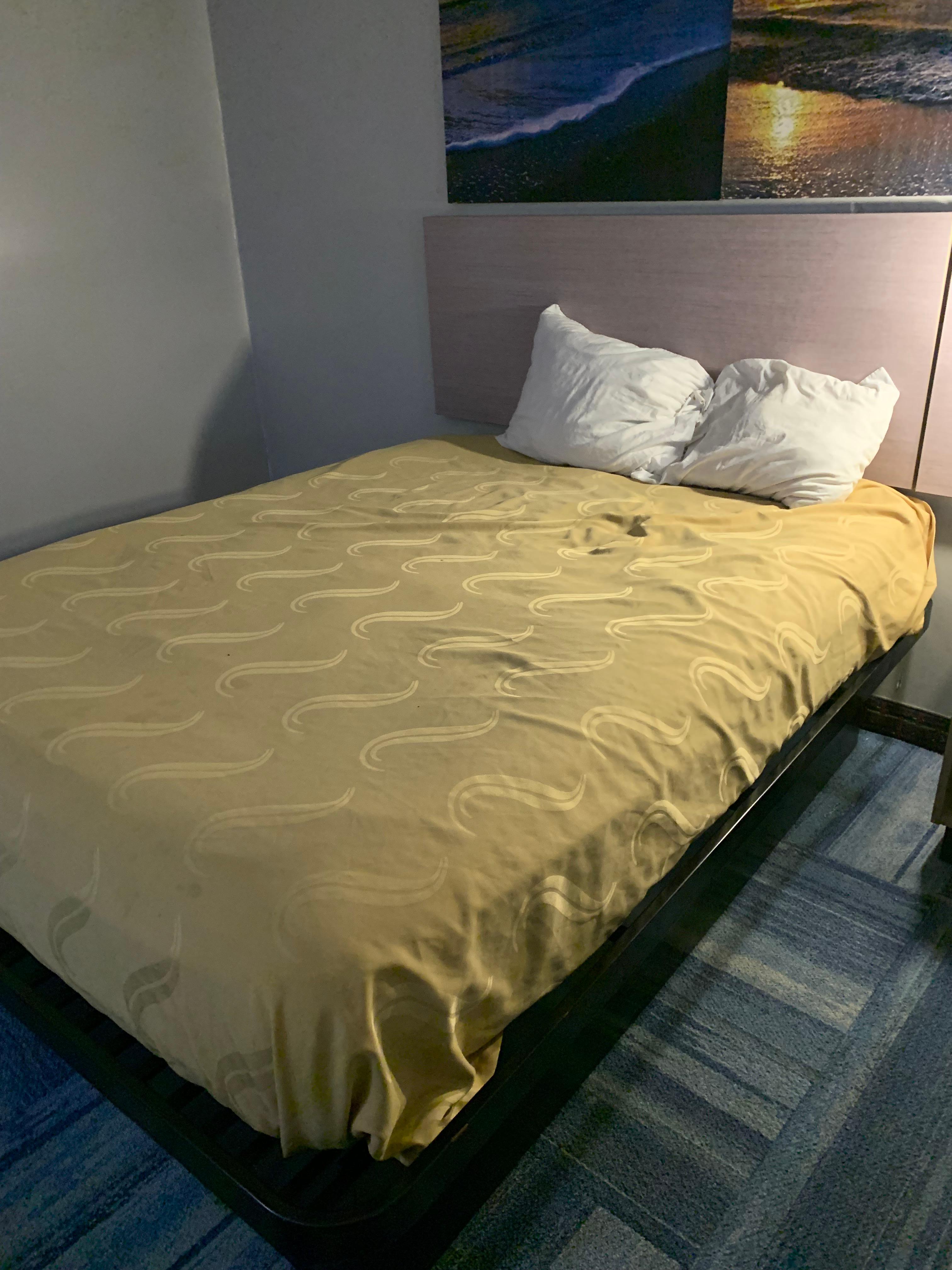 Metal bed with holes on sheet. Small lumpy pillows