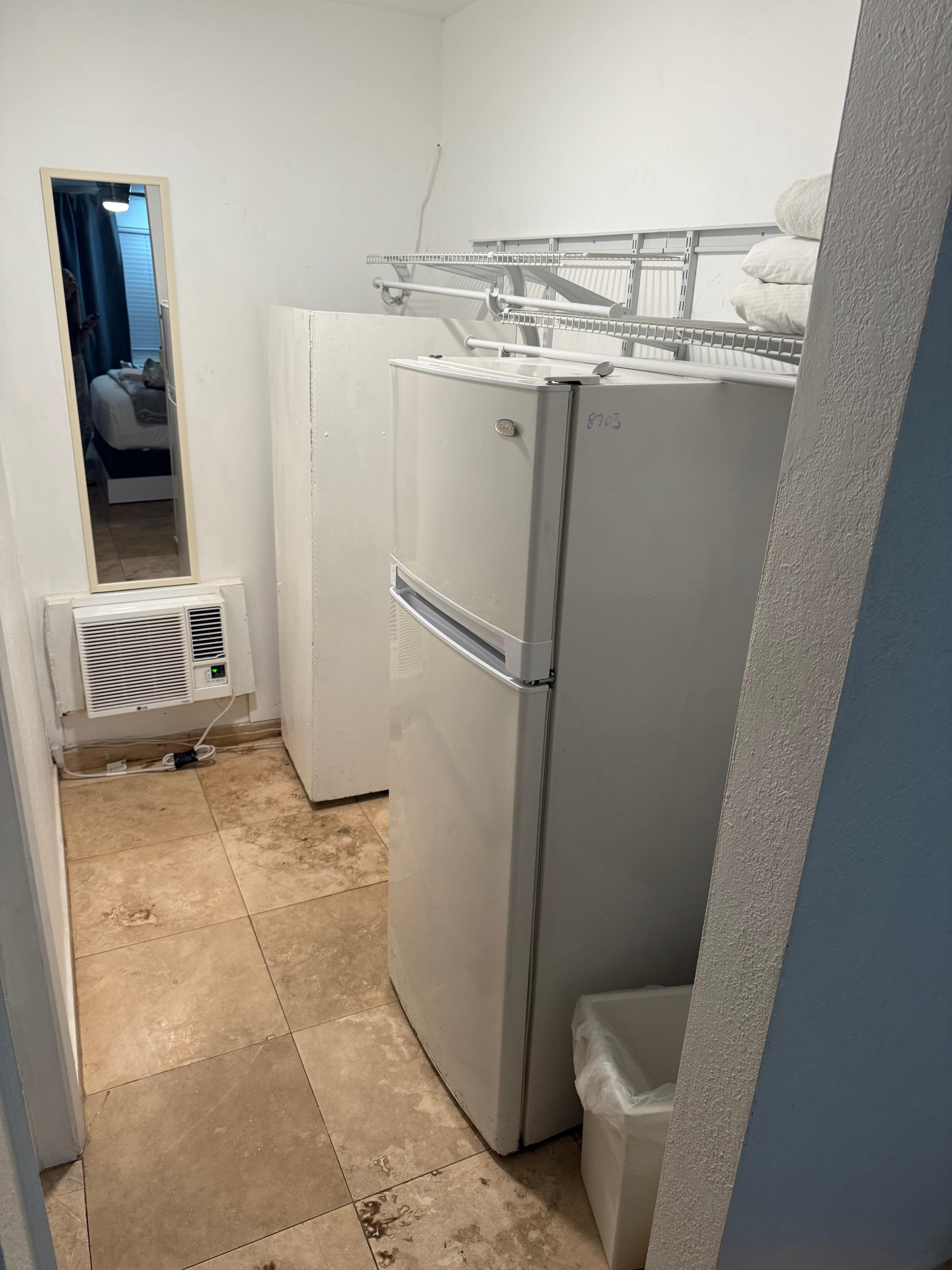 Fridge in closet holding up closet shelf with dirty spoons on top