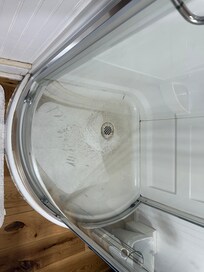 Dirty shower door and standing water and sand in shower base.