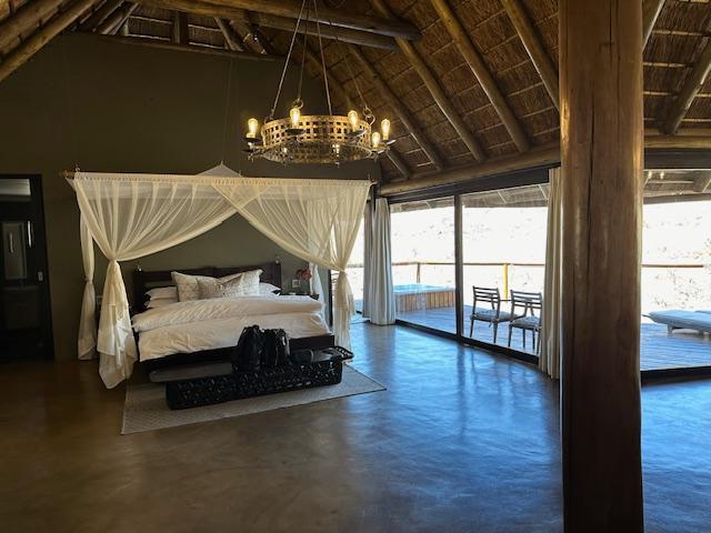 Bed, with mosquito nets, looks out over deck, with sun loungers and private hot tub