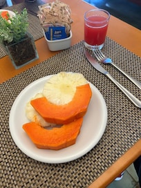 Prato colorido e refrescante com frutas da estação, servido com um copo de suco natural recém-preparado. Uma opção leve e nutritiva para começar o dia com sabor e vitalidade.