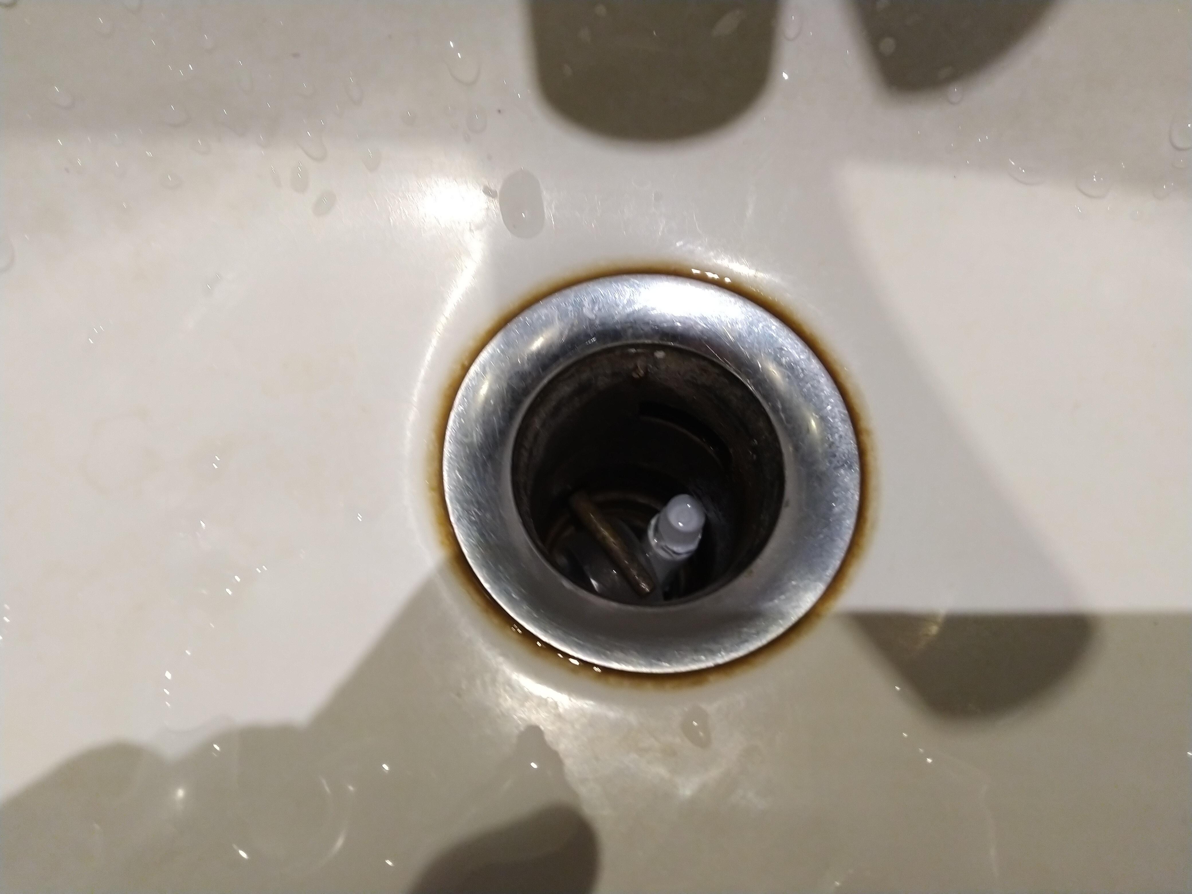 Wastafel tidak ada saringan dan terlihat ada pasta gigi dan tutup botol di dalam saluran pembuangan.