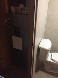 This is the fridge with the kitchen dishes on top of it, right next to the bathroom