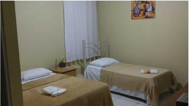 Foto do quarto 12 no site da Pousada, atrás da cama de solteiro tem 2 degraus de acesso a porta trancada atrás da cortina.