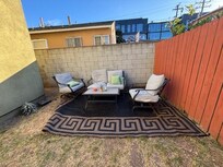 Outdoor seating area with ripped cushions, dirty rug in dirt yard.