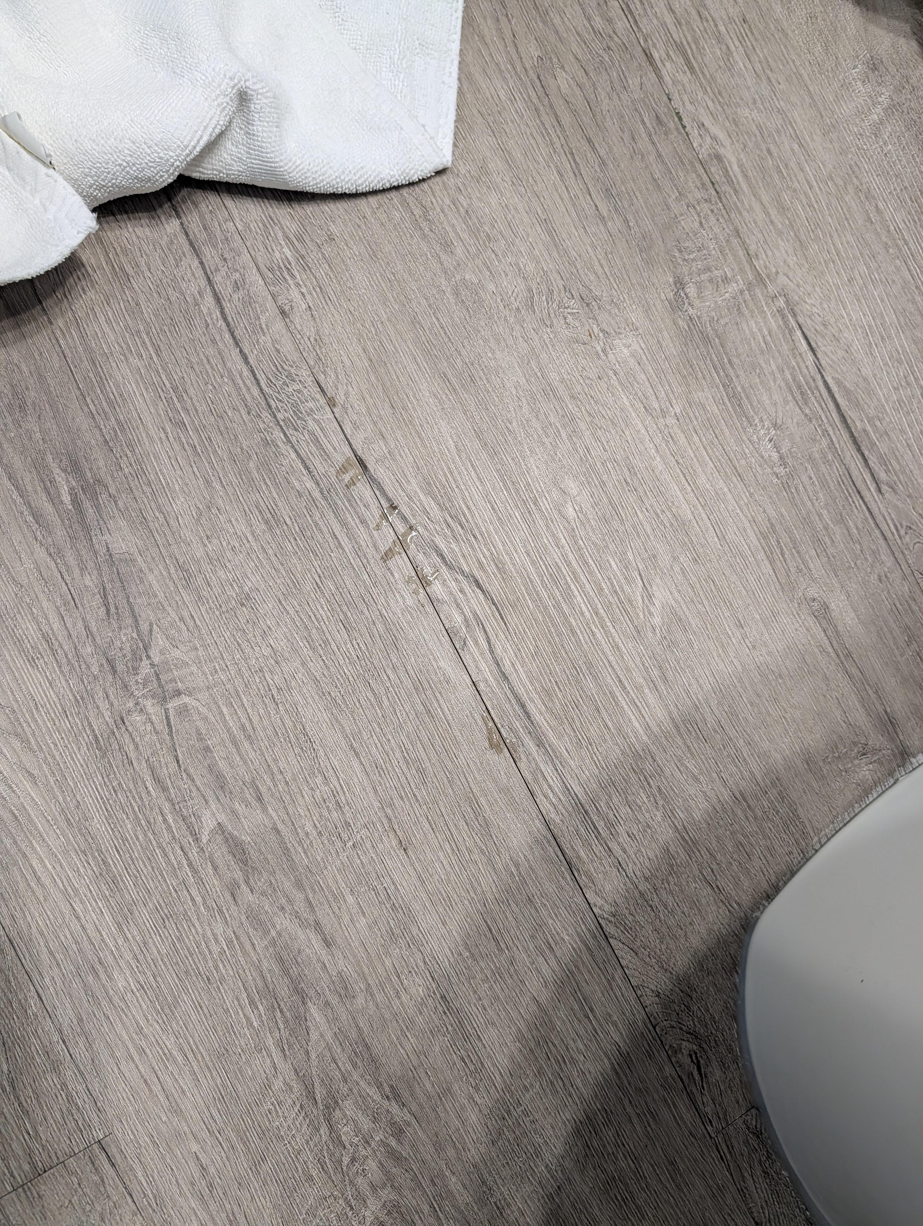 Small puddles of water leaking up from floorboards around toilet. 