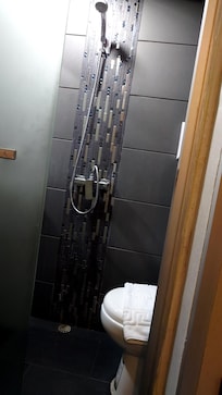 浴室。すりガラスの後ろに洗面台あり。浴室の床に勾配がないためシャワー後に溜まっている水を流す必要あり。浴室内にタオル類を干す場所もない。