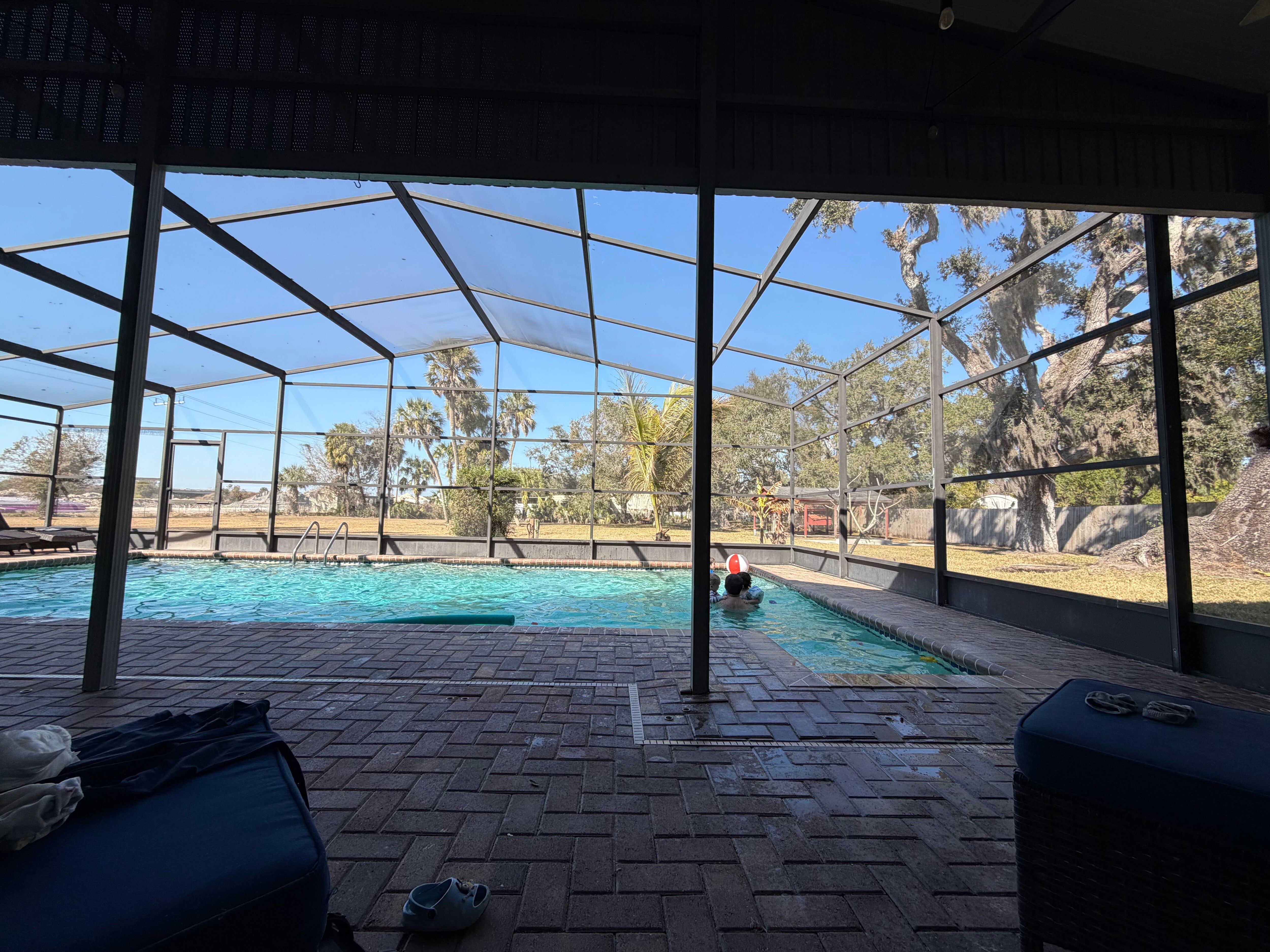Huge covered pool area with lounge chairs, table and chairs, and a patio box with pool floats/goggles and sand toys for the beach