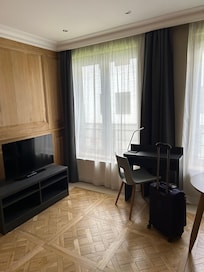 The living room with small desk, small table, and TV. The kitchenette is to the left behind closet doors, not pictured.