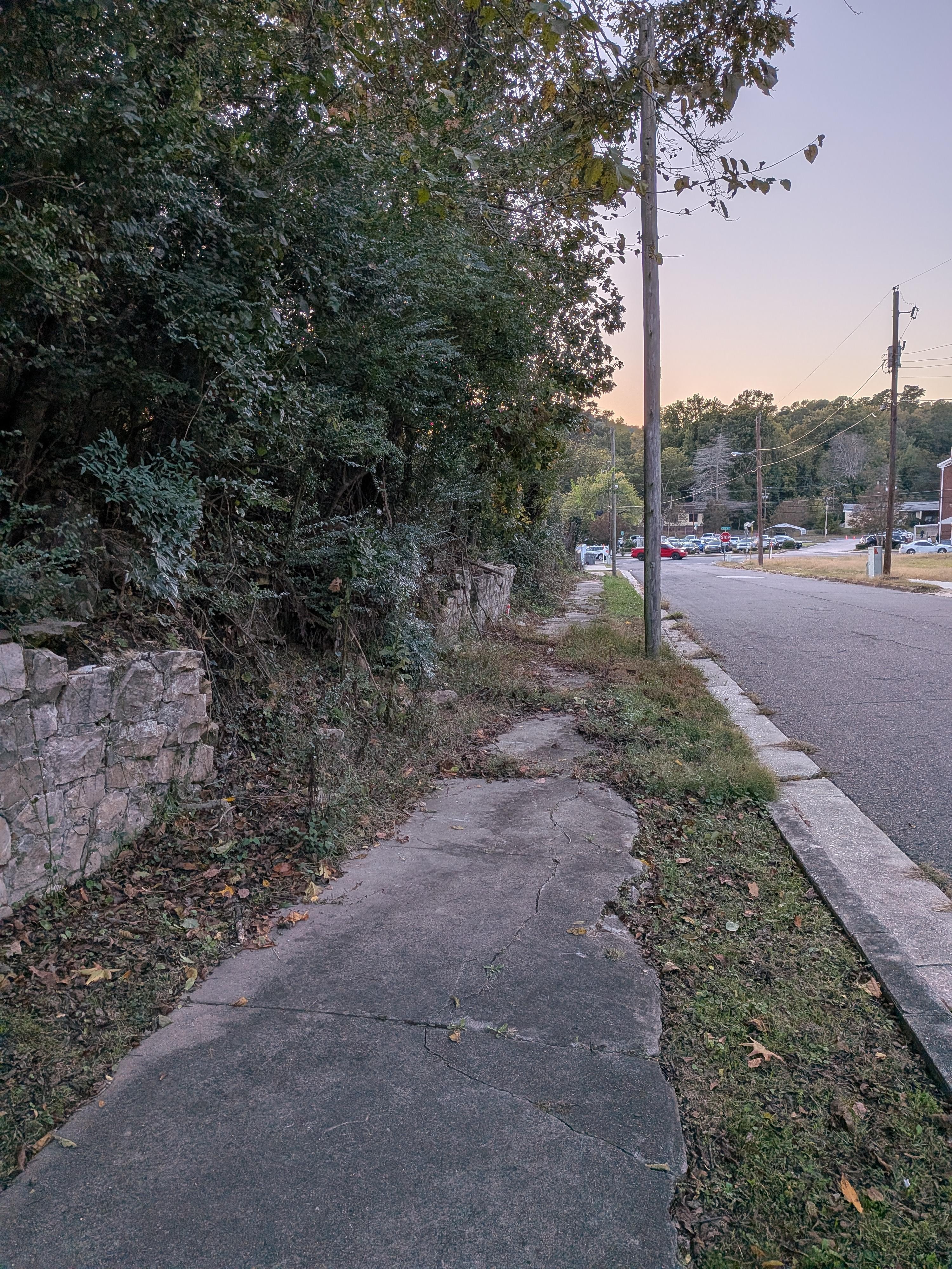 Damaged sidewalk on neighboring property near sunset. Street is well-lit at night.