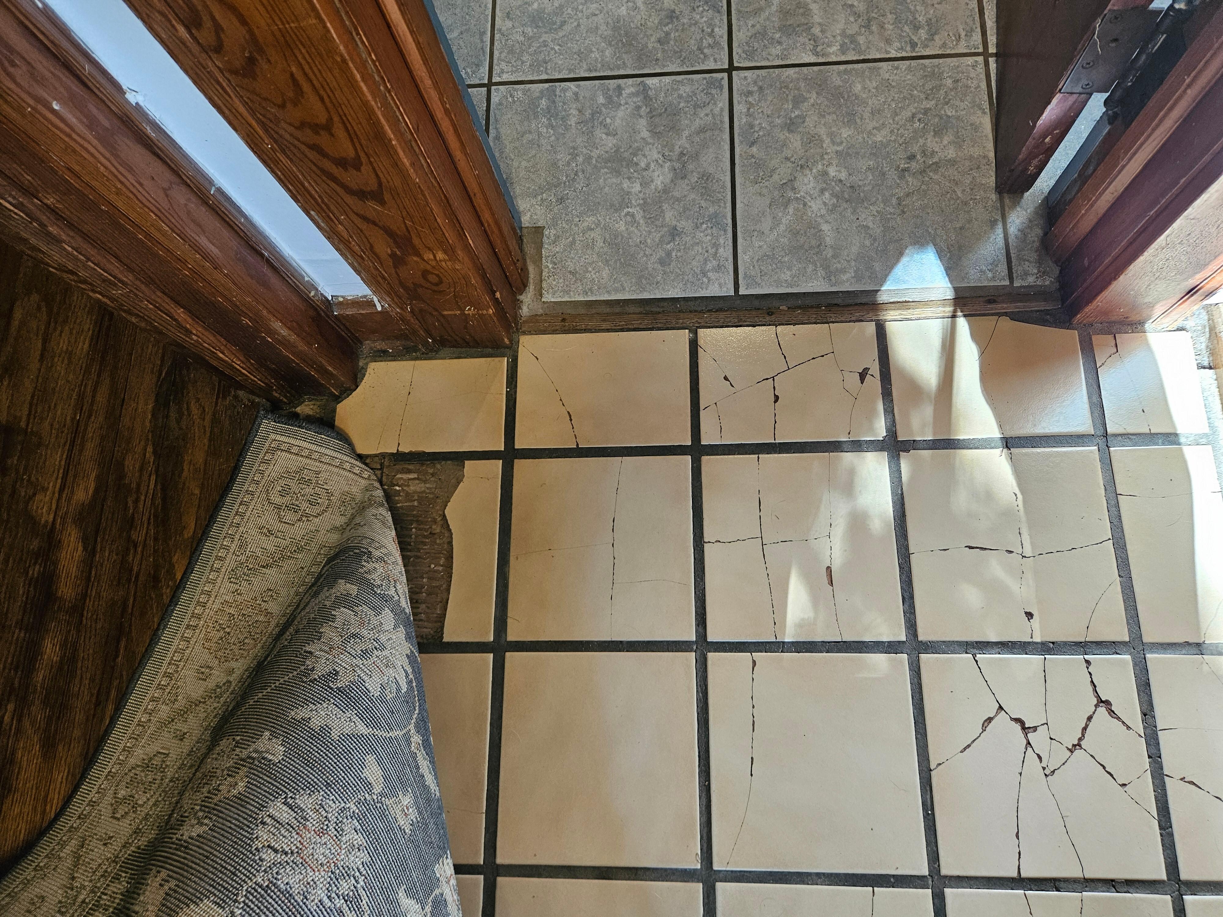 Broken and missing floor tile outside of the bathroom also covered with a throw rug