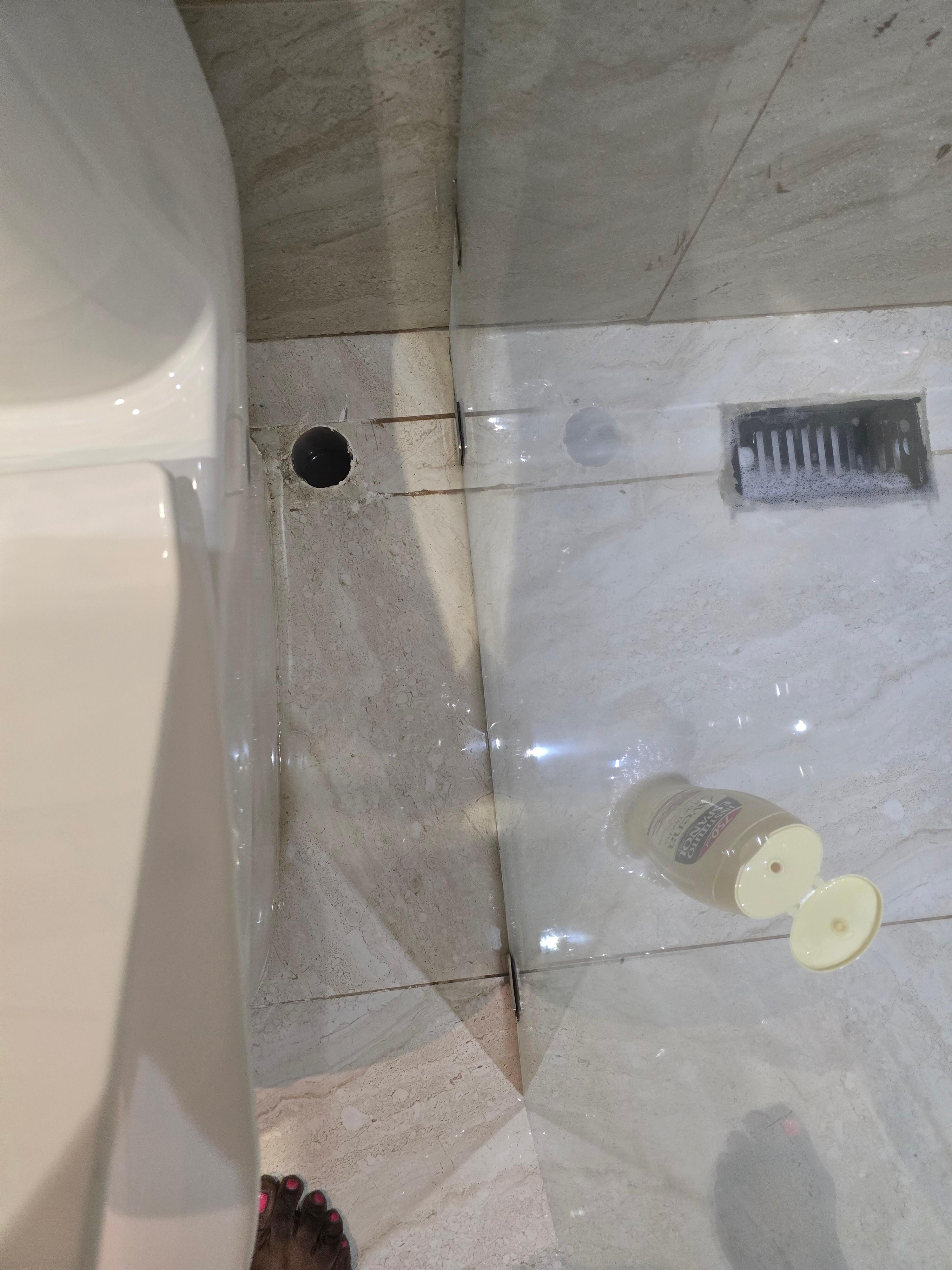 The hole in the floor is where the toilet paper holder should be. Looks like it was intentionally removed.  