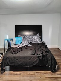 In the listing, the bedroom has 2 end tables and 2 lamps, as well as a shelf. This room has a bed and a stool.