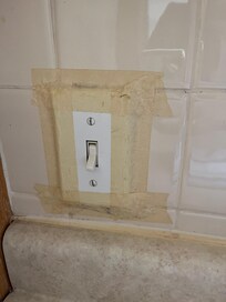 Light switch secured with masking tape adjacent to kitchen sink