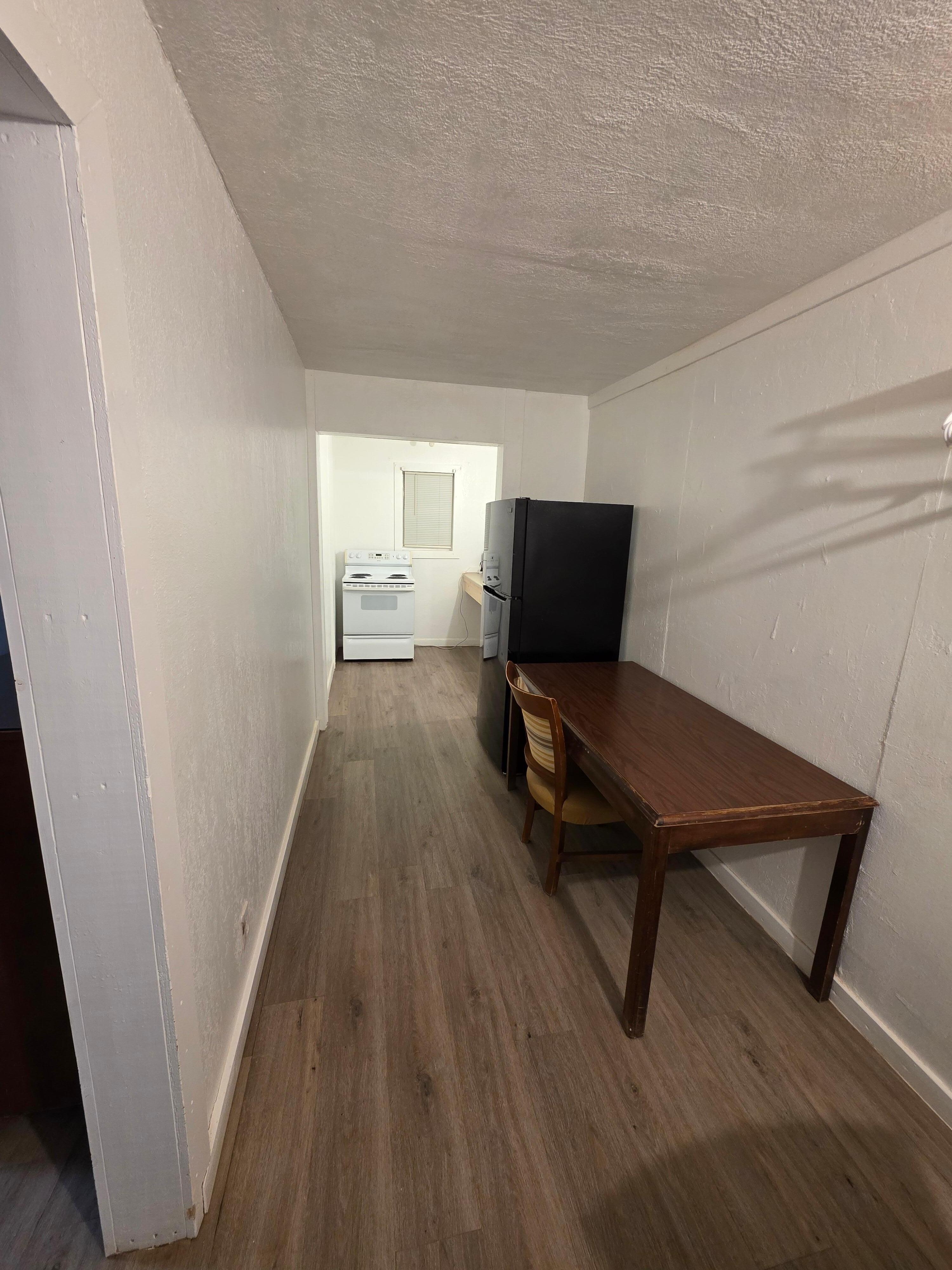 Two desks, a hanging rack, a full-size fridge, sink, and electric stove.