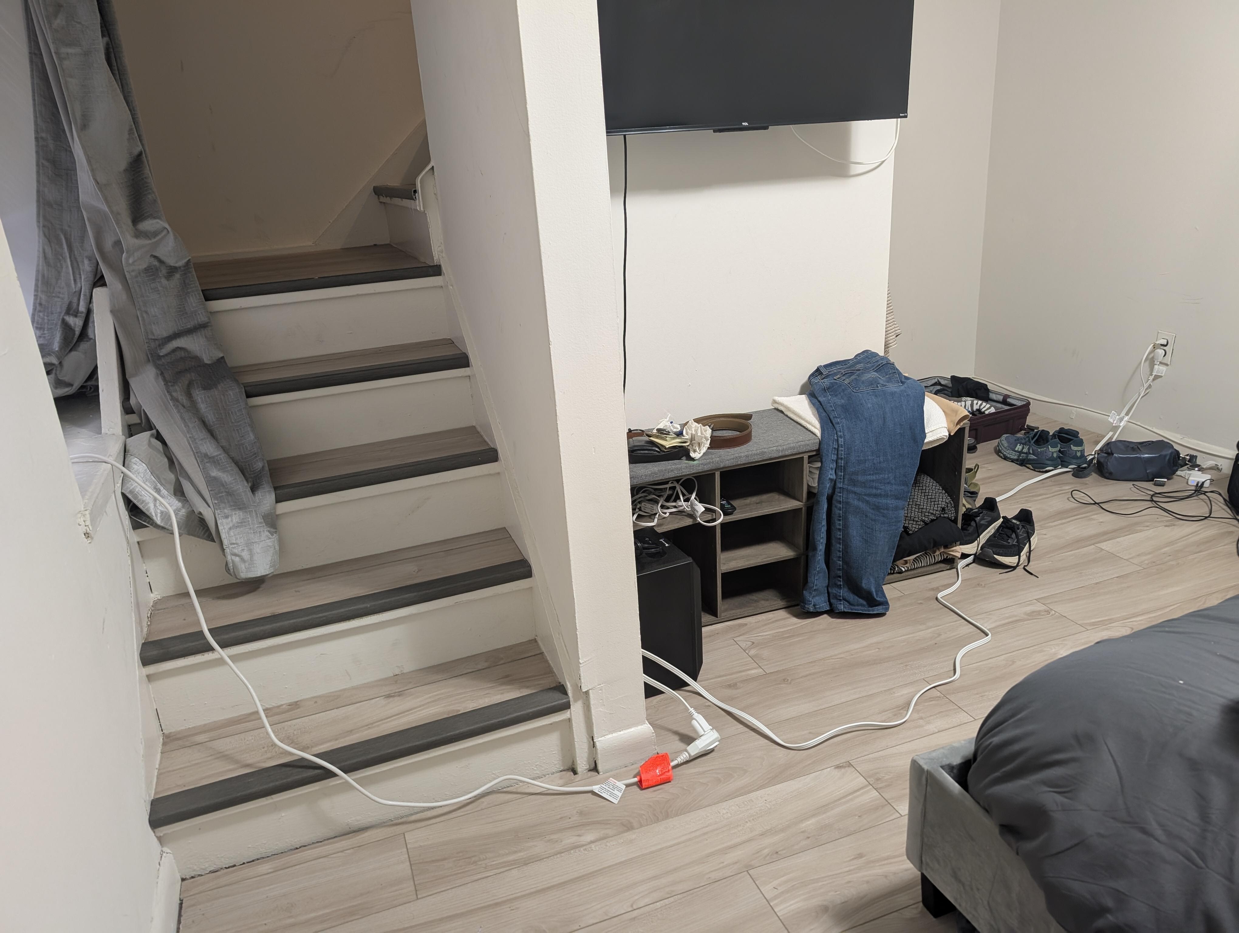 Stairs leading to second bedroom with loose electric cord over steps and across the room presenting a fall hazard if not a code violation.