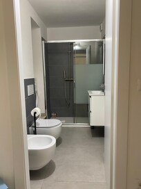 Linke Seite zwischen Toilette und Dusche steht die Waschmaschiene in einer Nische