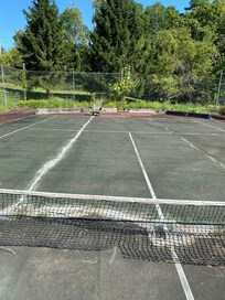 Tennis court with old gardens in every corner and broken net and white concrete to fill up huge cracks.