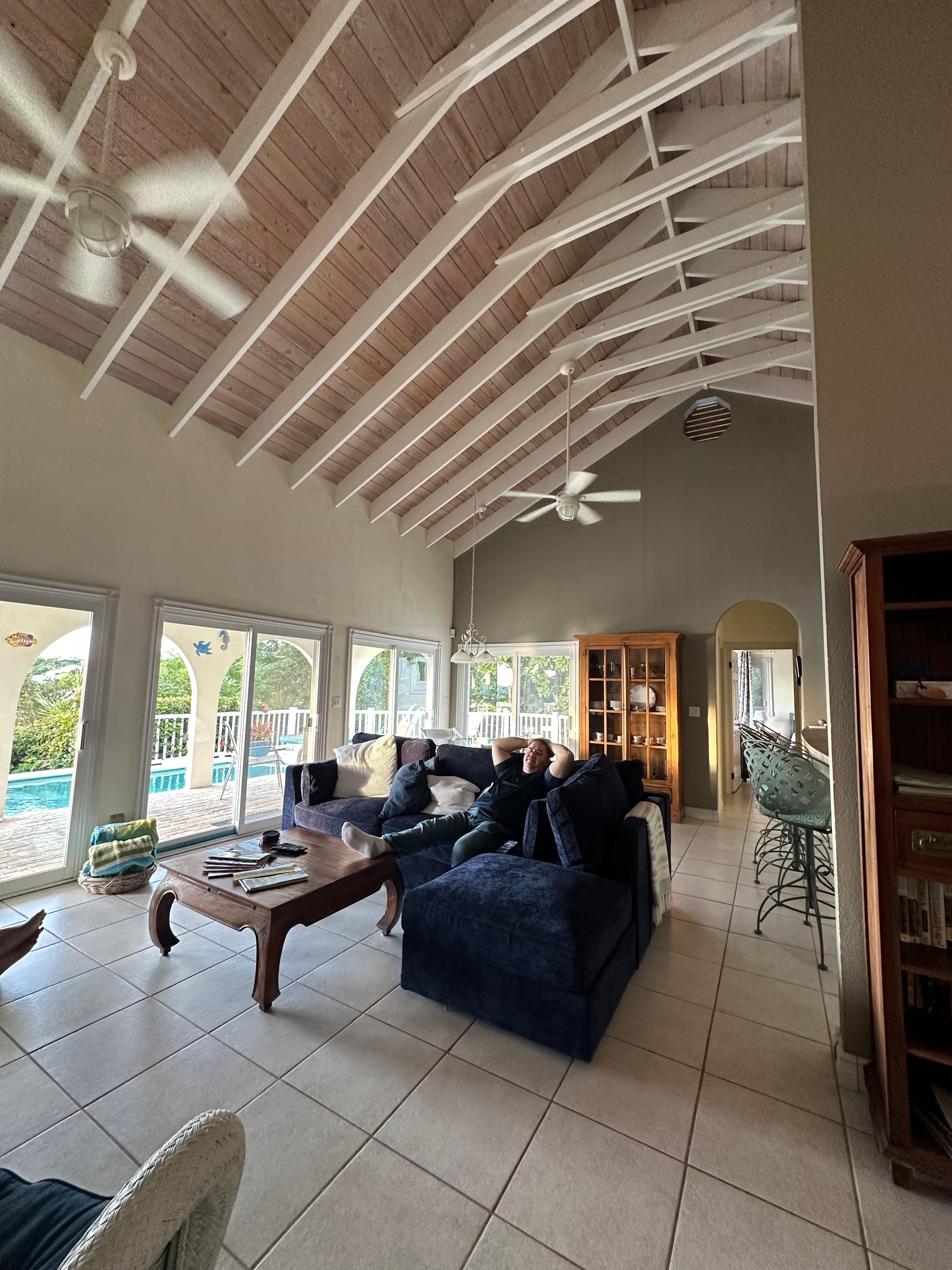 Living room area with a dining table, sectional couch, wicker chairs, tv, games, books, island magazines 
